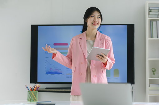 Smiling millennial Asian female office worker working with digital tablet for tax audit reports or financial statement in a meeting room