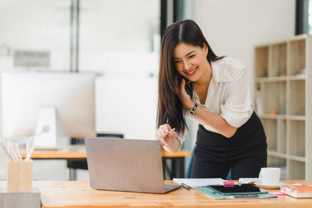 istock Busy professional businesswoman engages in a phone conversation while using laptop in a contemporary office workspace. 2148562547