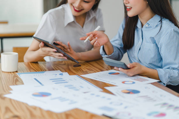 istock Two colleagues engaged in business analytics, using digital tablets over financial charts. Colleagues Collaborating with Tablets on Business Analytics. 2148563163