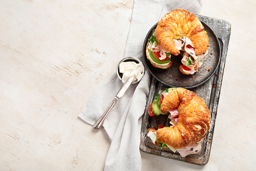 Salted healthy breakfast on light background. Fresh sandwich with croissant bun, cream cheese, avocado, ham. Top view, copy space