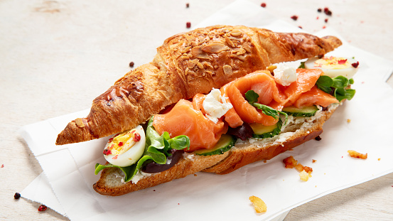 Salted healthy breakfast on light background. Fresh salmon croissant with cream cheese, cucumber, egg and salad.