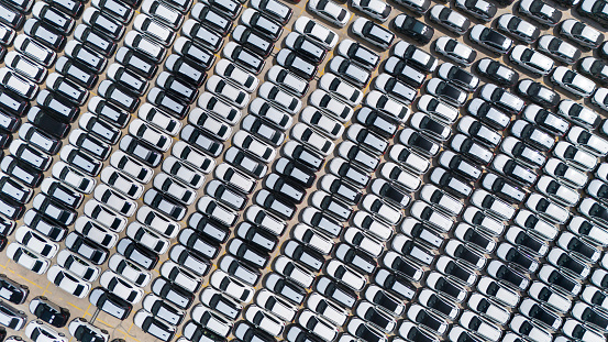 Aerial view rows of new cars waiting to be dispatch and shipped, new cars lined up in a commercial port for import export.