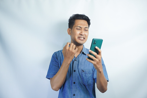 Asian man wearing blue shirt using mobile phone. standing watching messages on mobile phone Symptoms of young man sad and crying receiving bad news message