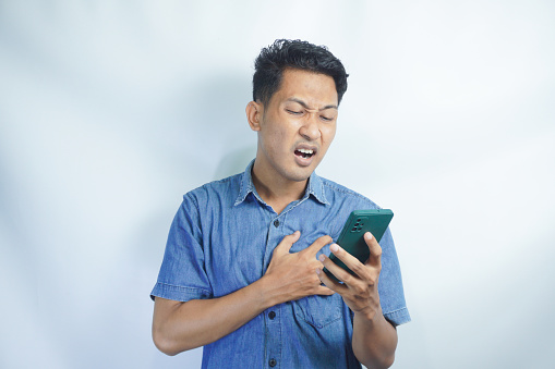 Asian man wearing blue shirt using mobile phone. standing watching messages on mobile phone Symptoms of young man sad and crying receiving bad news message