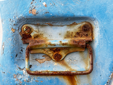 A rusted metal handle is attached to a blue surface. The handle is old and worn, with rust covering its surface. Scene is one of decay