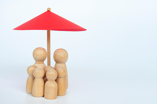 Red toy umbrella and wooden family doll figures a white background. Life insurance coverage concept.