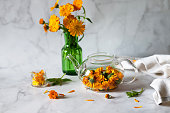 Cup of marigold tea and calendula flowers outdoors on green background.