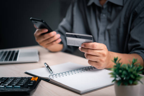 Man with credit card and smartphone finalizes a transaction, with a calculator and notepad nearby. online payment transaction e commerce shopping internet finance banking business concept. un hombre con tarjeta de crédito y teléfono inteligente finaliza una transacción, con una calculadora y un bloc de notas cerca. transacción de pago en línea, comercio electrónico, compras, finanzas por internet, concepto de negocio, banca.