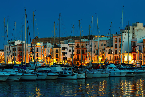View of the yachts and illuminated houses in the evening in the town of Eivissa, Ibiza, Spain.