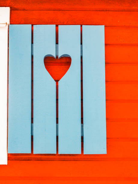 A close view of bright blue shutters with an adorable heart-shaped cutout, set against the warm red facade of a traditional Swedish home. The contrasting colors and charming design evoke a sense of coziness and cultural aesthetics found in Sweden.
