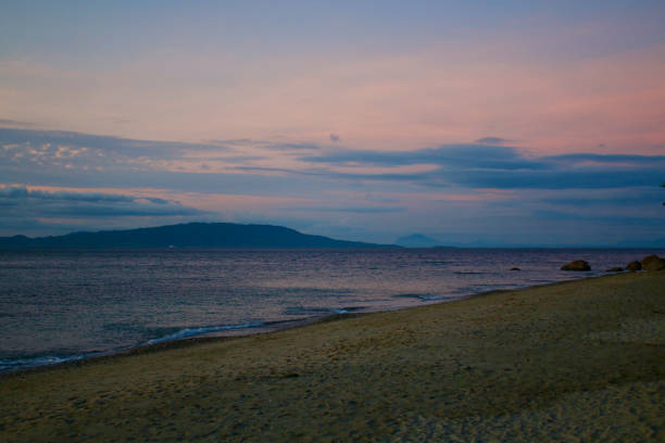 View of the beach, calm sea and tropical island on the horizon in the evening.