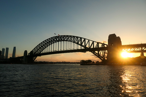 The Sydney Harbour Bridge on an afternoon in Autumn.  In the left distance are skyscrapers in the central business district, with the closest one to the bridge being the Crown Casino in Barangaroo. This image was taken from the foreshore of Sydney Harbour at Kirribilli at sunset on 13 April 2024.