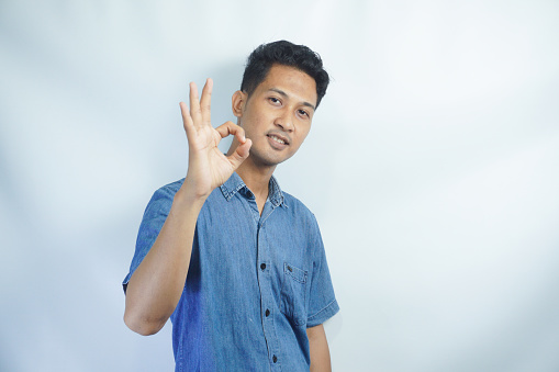 Young handsome man wearing blue shirt over white background smiling positive doing ok sign with hand and fingers. Successful expression.