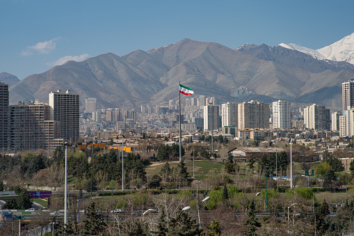 The city of Tehran with the waving Iranian Flag in the middle and the mountains in the background