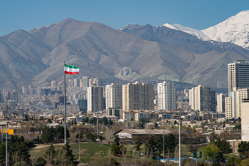 Panoramic view of the city of Tehran with the waving Iranian Flag and the mountains in the background