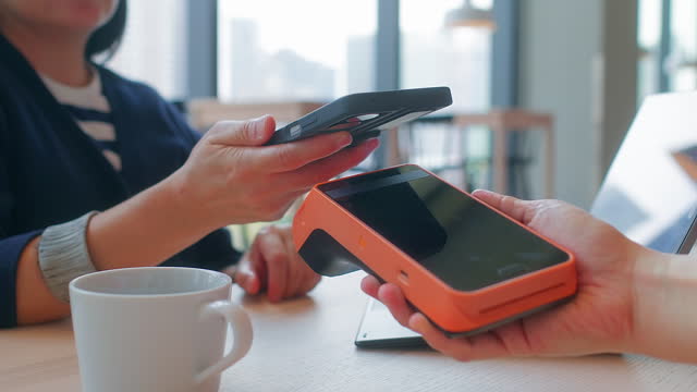 woman contactless payment with mobile phone while working remotely at coffee shop