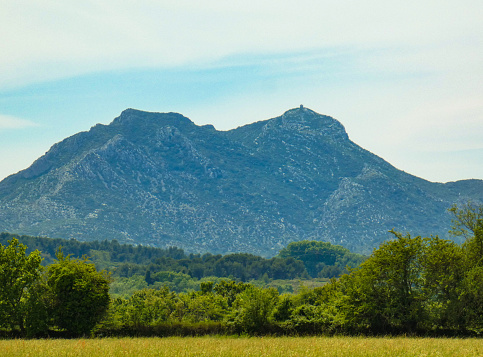Breathtaking landscape photo with a meadow and the vegetation of provencal nature and in the background the majestic Opies mountain in the Alpilles chain. This photo was taken in Provence in France.