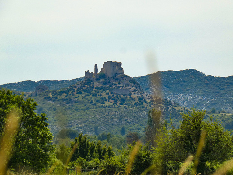 Photo of an idyllic landscape with provencal nature and the castle of queen Jeanne (or castle of Roquemartine) perched on top of its hill in the Alpilles. This photo was taken in Provence in France.