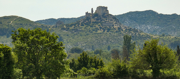 Photo of a panoramic landscape with provencal nature and the castle of queen Jeanne (or castle of Roquemartine) perched on top of its hill in the Alpilles. This photo was taken in Provence in France.