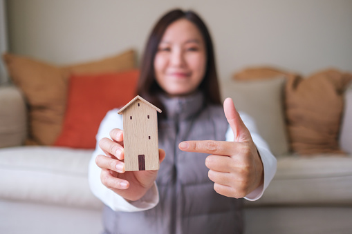 Blurred image of a young woman holding and pointing finger at a wooden house model