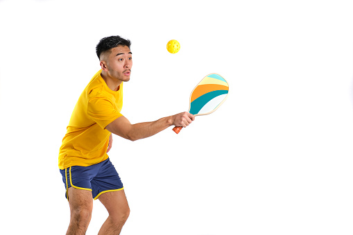 oriental young man in yellow t-shirt playing pickleball on white background