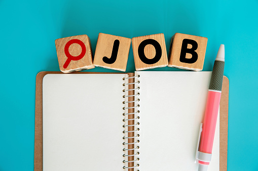 JOB word with magnifying Glass Icon on Toy blocks and blank spiral notebook. Blue background.