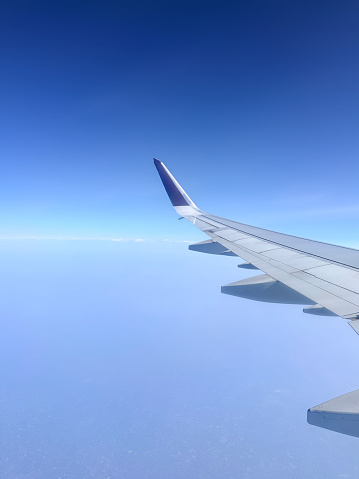 Stock photo showing the wing of a plane pictured through the airplane window with views of cumulous clouds.