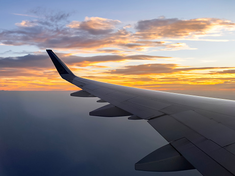 Stock photo showing the wing of a plane pictured through the airplane window with views of sunset and cumulous clouds.