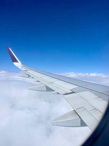 Stock photo showing the wing of a plane pictured through the airplane window with views of cumulous clouds.