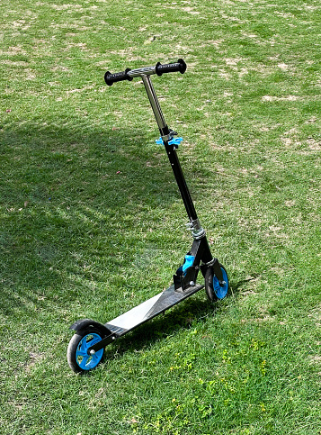 Stock photo showing close-up view of a children's toy vehicle of a kick scooter left standing on a green grass, mown lawn.