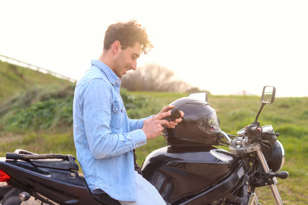 istock Curly haired Caucasian young man sitting on his motorcycle using mobile phone smiling 2148582450