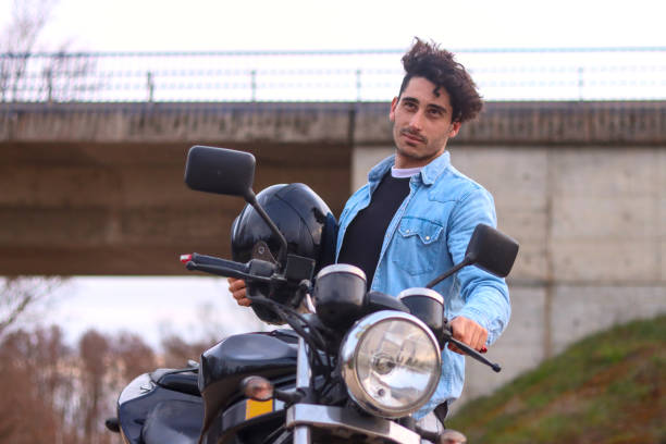 istock Curly haired Caucasian young man holding his motorcycle and helmet 2148582458