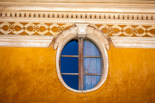 Detail of oval window on old yellow facade in a house in the old town of Caravaca, Region of Murcia, Spain