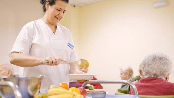 istock Smiling cook serving food to old people in a geriatric 2148583213