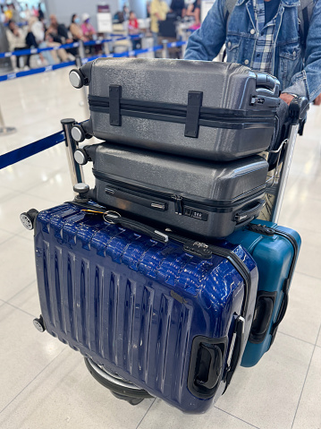 Stock photo showing close-up view of a luggage cart piled with suitcases being wheeled through an airport departure area.