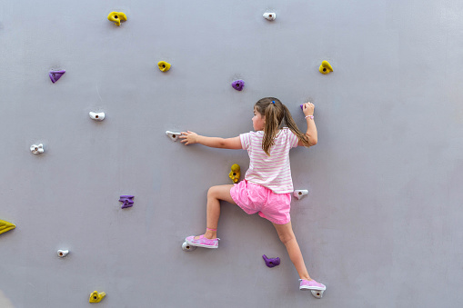little girl climbing a rock wall outdoor in public park. High quality photo