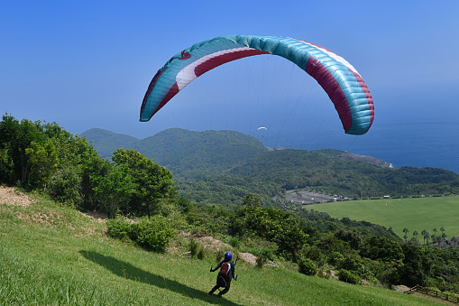 August 6, 2021 - Ager, Spain: profesional Paraglider pilot running and jumping taking off from the mountain while other people are looking at him
