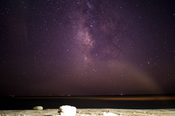 A breathtaking coastal scene as the Milky Way adorns the night sky over the sea and mountain, creating a serene and cosmic marvel.
