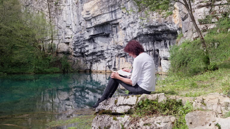 SLO MO Senior woman sitting on a rock and reading a book.