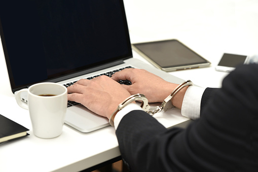 Hands of an office worker operating a laptop while wearing handcuffs or chains in the office