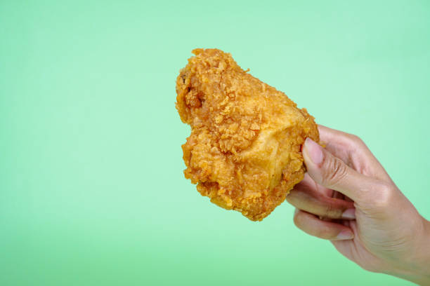 istock Female hand holding fried chicken on green background. 2148586922