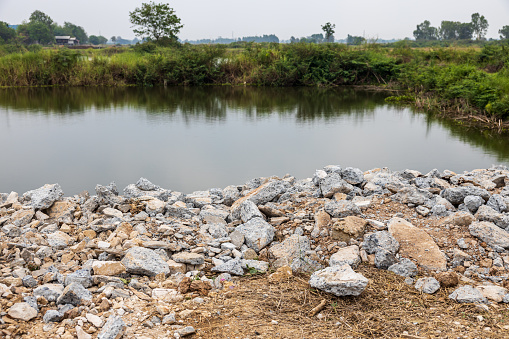 A view of piles of broken concrete scrap taken from road demolition left on a mound near the edge of a pond, a common sight on agricultural land in the Thai countryside.