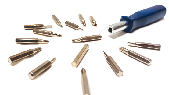 A close-up shot of the screwdriver bit facing the screwdriver handle. piles of steel screwdrivers of different types and sizes, isolated on a white background.