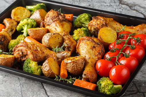 BBQ baked chicken drumsticks with seasonal vegetables and rosemary close-up on a baking sheet on the table. Horizontal
