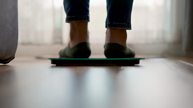 Close-up shot of female' s feet stepping on digital floor scales at home