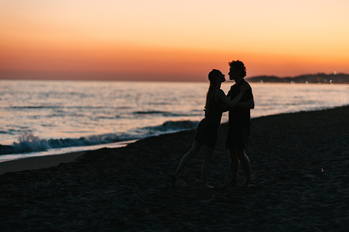 The silhouettes of a happy couple dancing by the sea at sunset, just before nightfall, holding hands