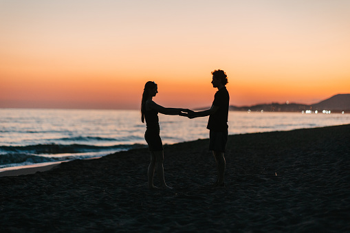 The silhouettes of a happy couple dancing by the sea at sunset, just before nightfall, holding hands