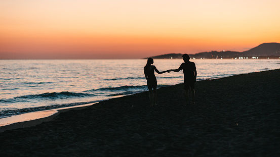 The silhouettes of a happy couple on a romantic walk by the sea at sunset, just before nightfall, holding hands. Ada Bojana, Crna Gora
