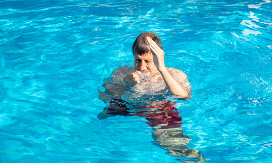 A man with a sore head from the sun floating in the water of a pool or spa. Blow to the head when jumping into the pool