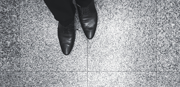 Man's Leg and leather shoes standing on the marble floor in black and white style with copy space. Human body part, Art and Abstract concept.